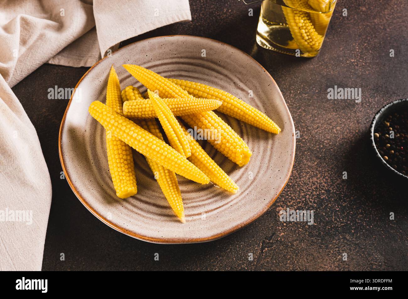 Portion of canned corn on the cob on a plate and in a jar on a table Stock Photo