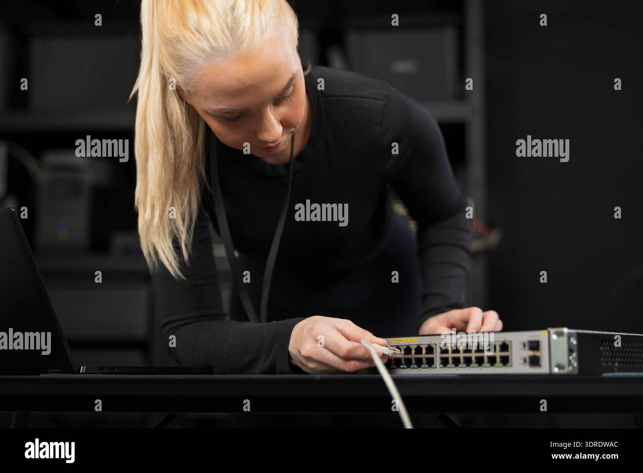 Professional female IT technician configuring a network switch in a modern office setting Stock Photo