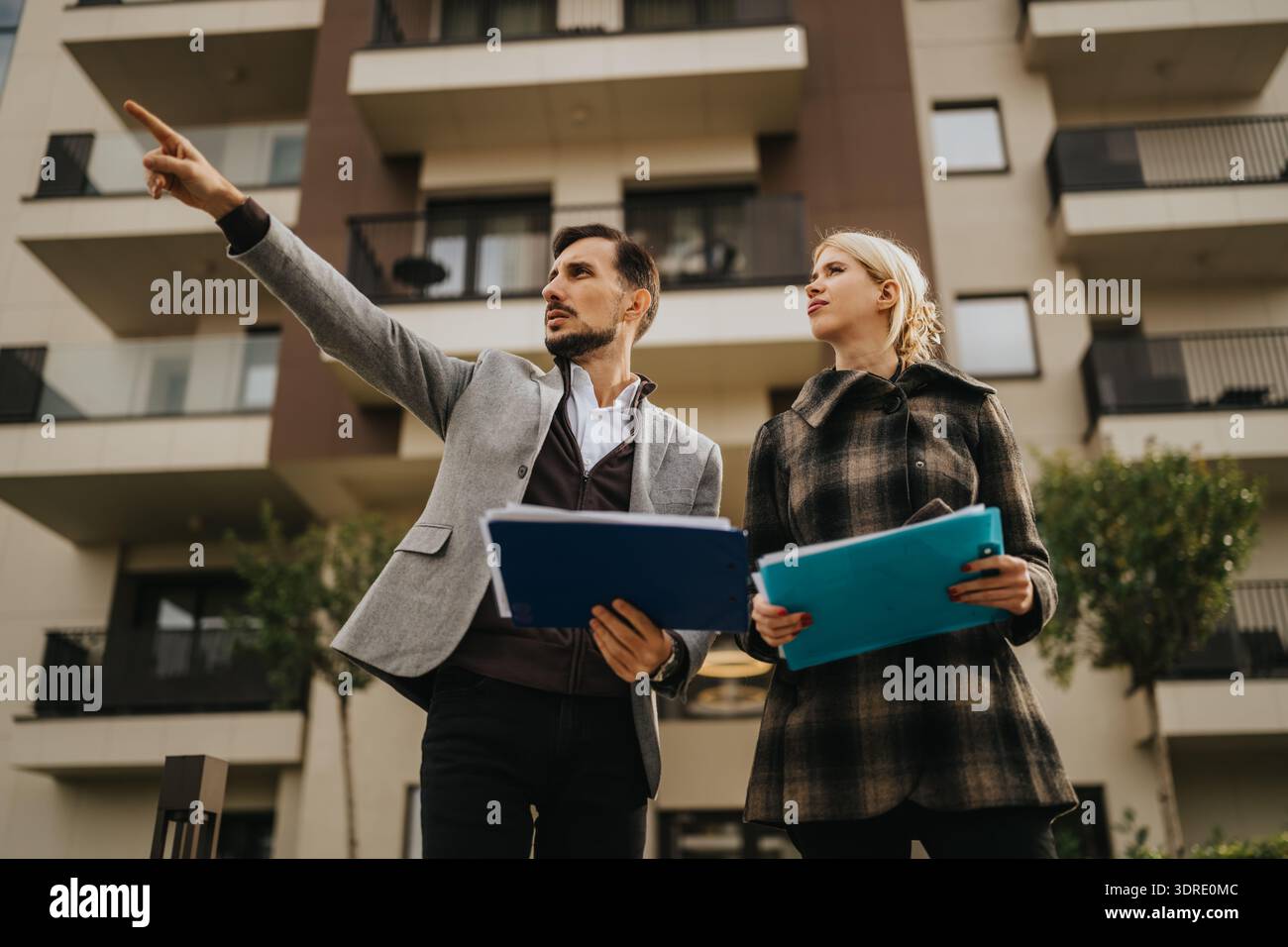 Business partners review plans outside a modern building, one points ...