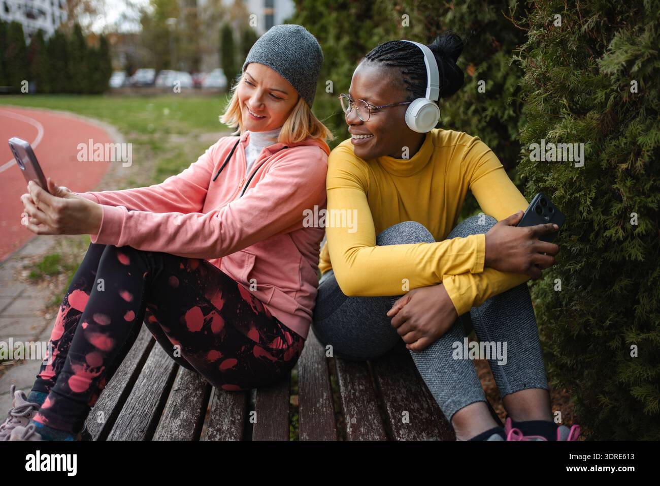 Diverse women friends resting on bench using smartphone Stock Photo