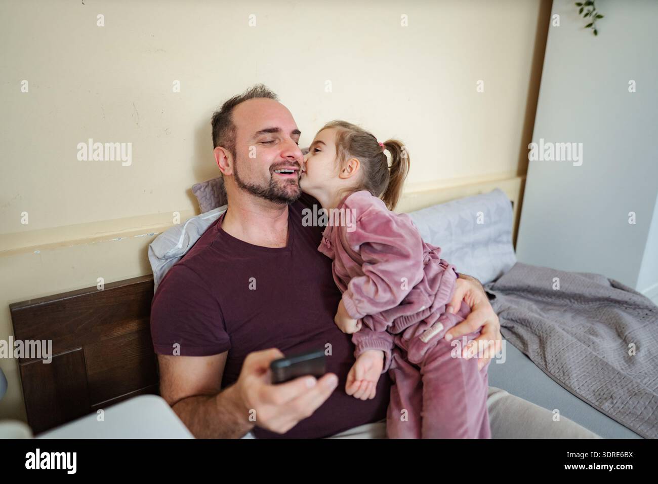 Happy father receiving daughter's kiss using smartphone Stock Photo