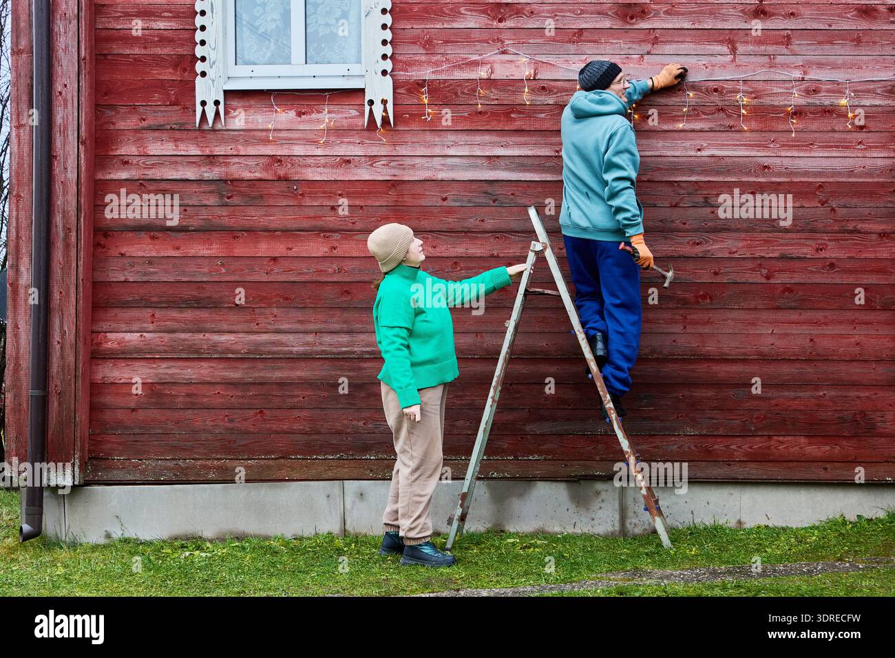 Installing string lights on facade of wooden farm building. Stock Photo
