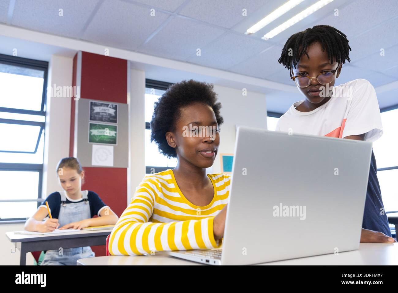 In school, diverse students collaborating on laptop while classmate writing in notebook Stock Photo
