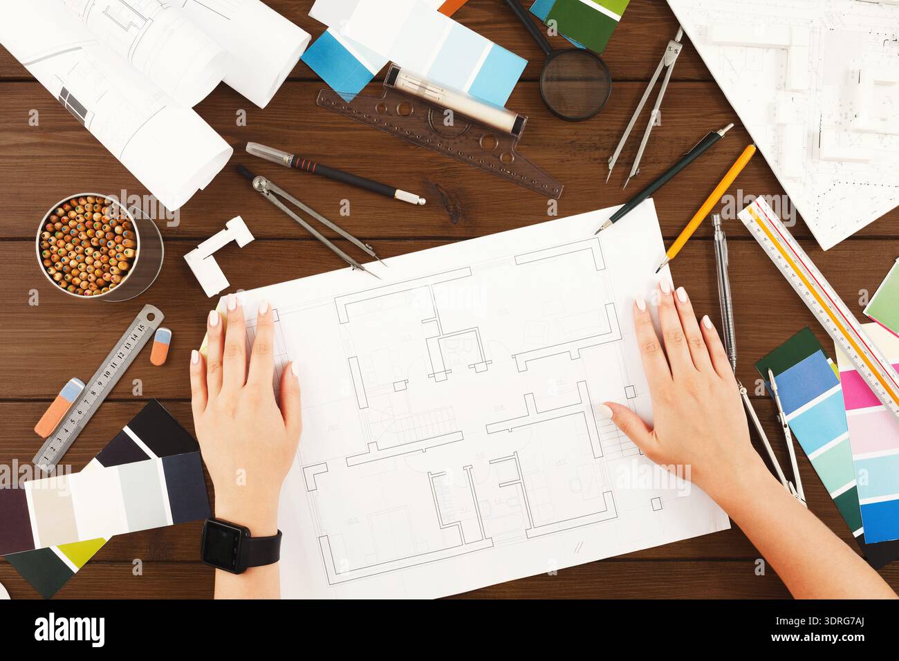 Hands Working on a Layout Plan With Various Colors and Tools Spread on a Wooden Table Stock Photo