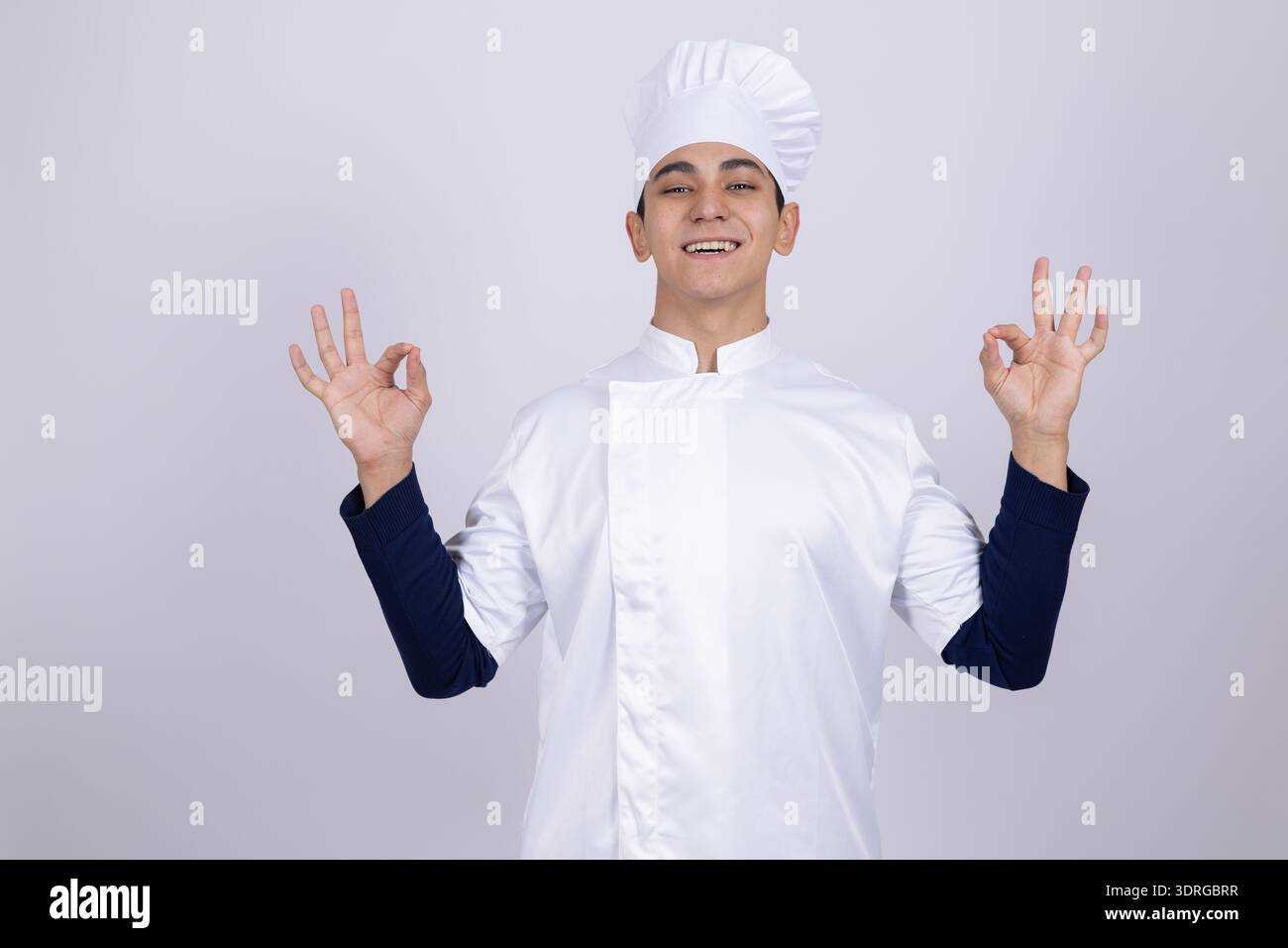 Smiling young chef in white uniform showing ok sign Stock Photo