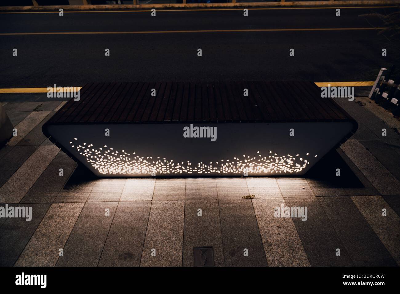 Modern illuminated bench on city sidewalk at night with glowing light dots and urban street background Stock Photo
