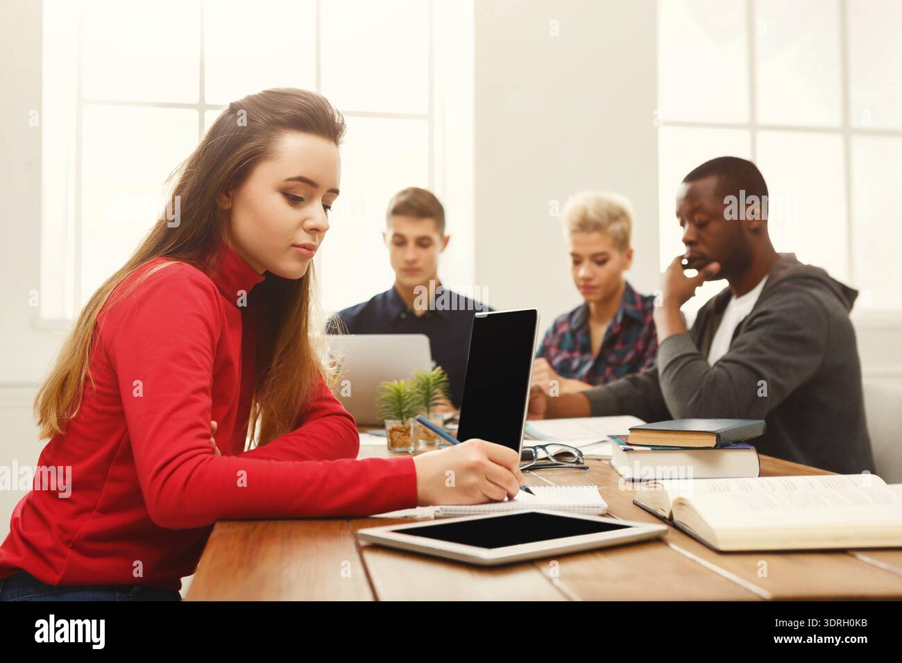 Students Engaged in Study Session With Digital Devices and Books Stock Photo