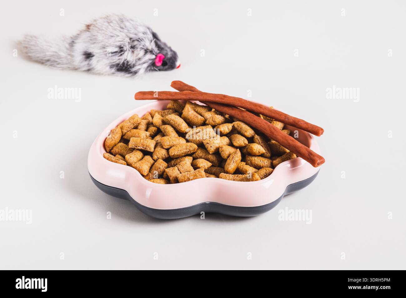 Bowl with dry cat food pellets and toy fluffy mouse on table Stock Photo