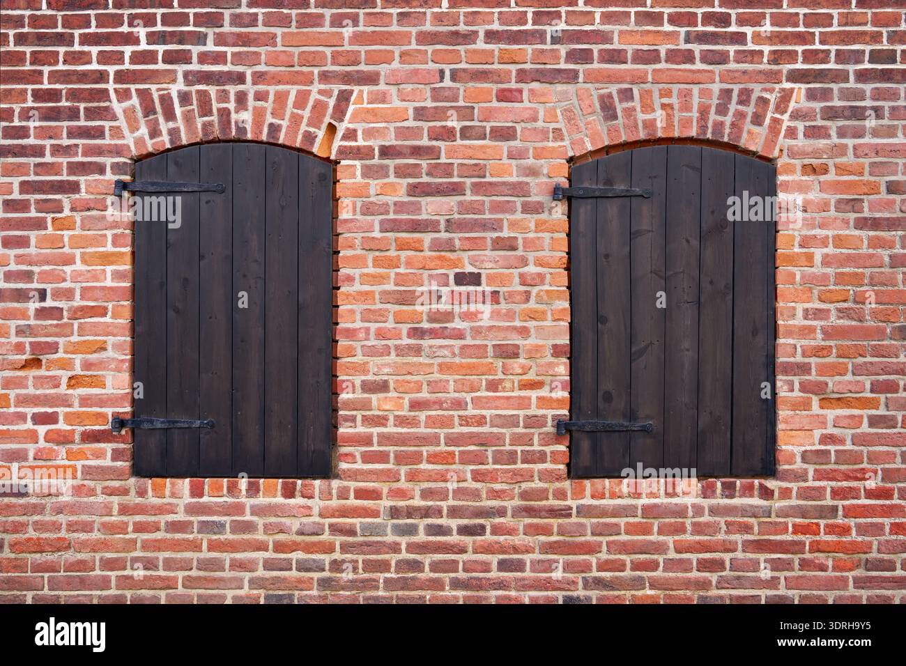 Two closed brown window shutters in a red brick facade Stock Photo