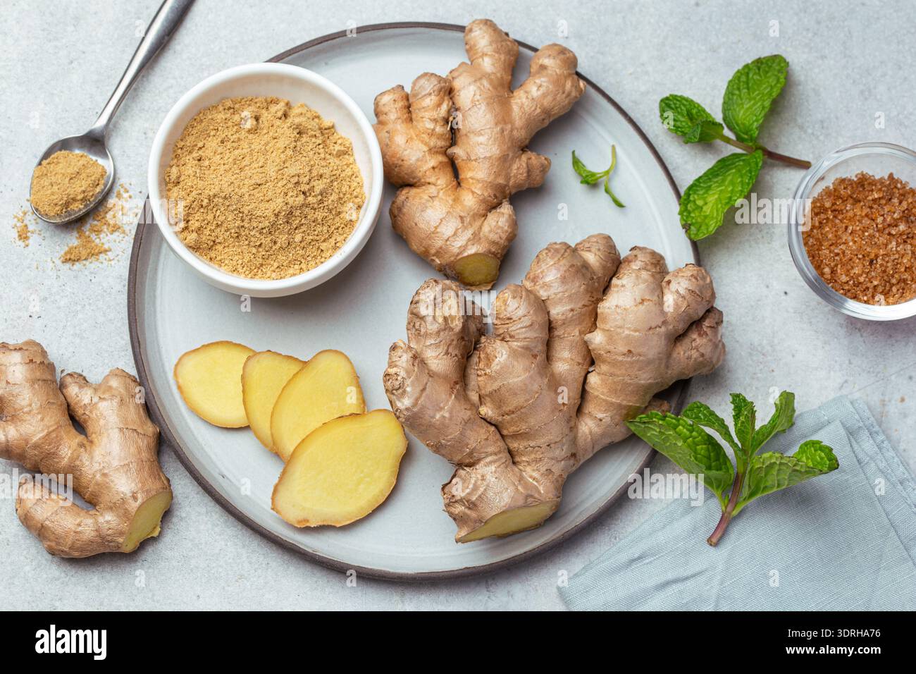 Sliced fresh ginger root,  ginger powder and mint leaves on plate, top view Stock Photo