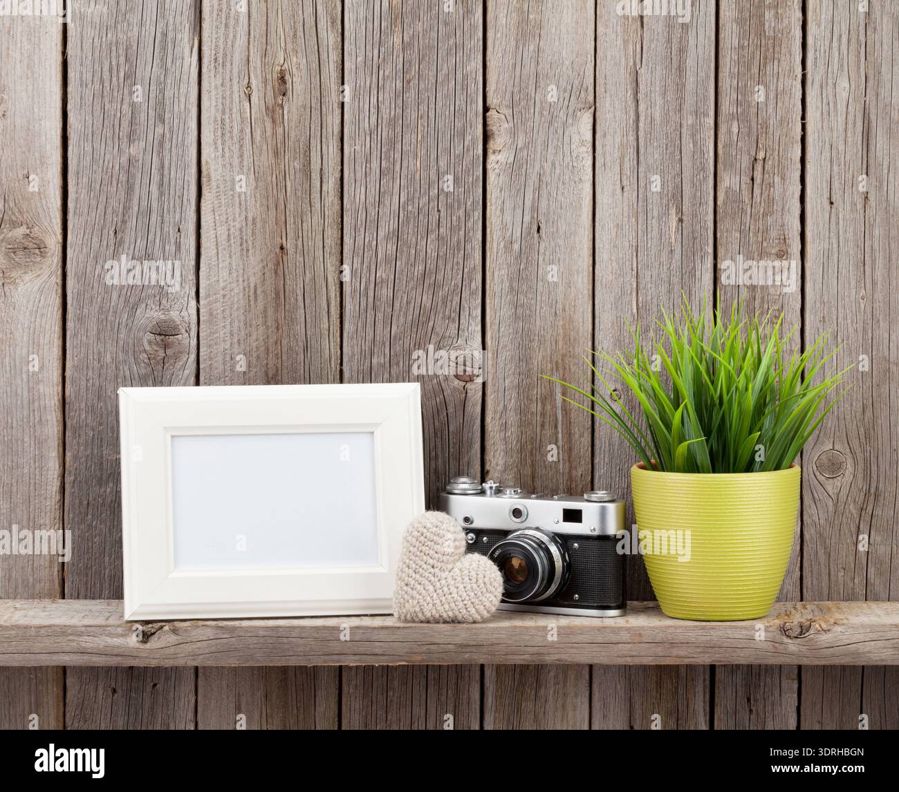 Blank photo frame, heart gift, camera and plant on shelf in front of wooden wall Stock Photo