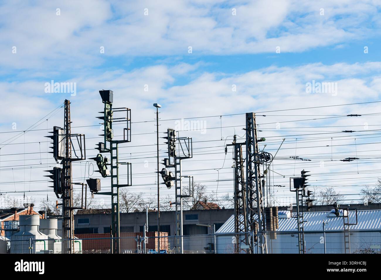 Railway signals stand tall against a blue sky with clouds. Nearby ...