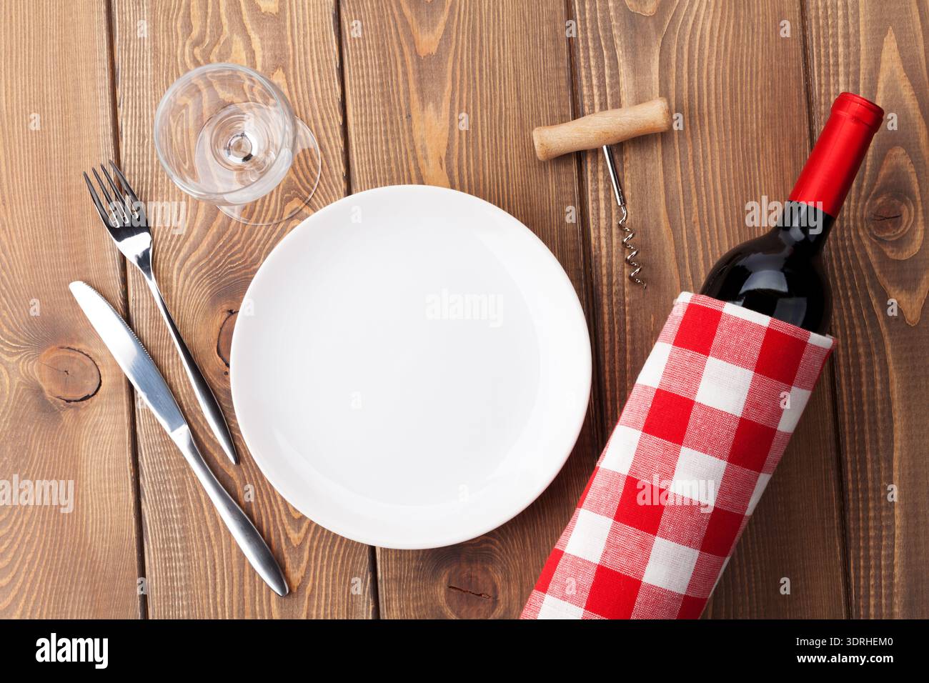 Table setting with empty plate, wine glass and red wine bottle Stock Photo
