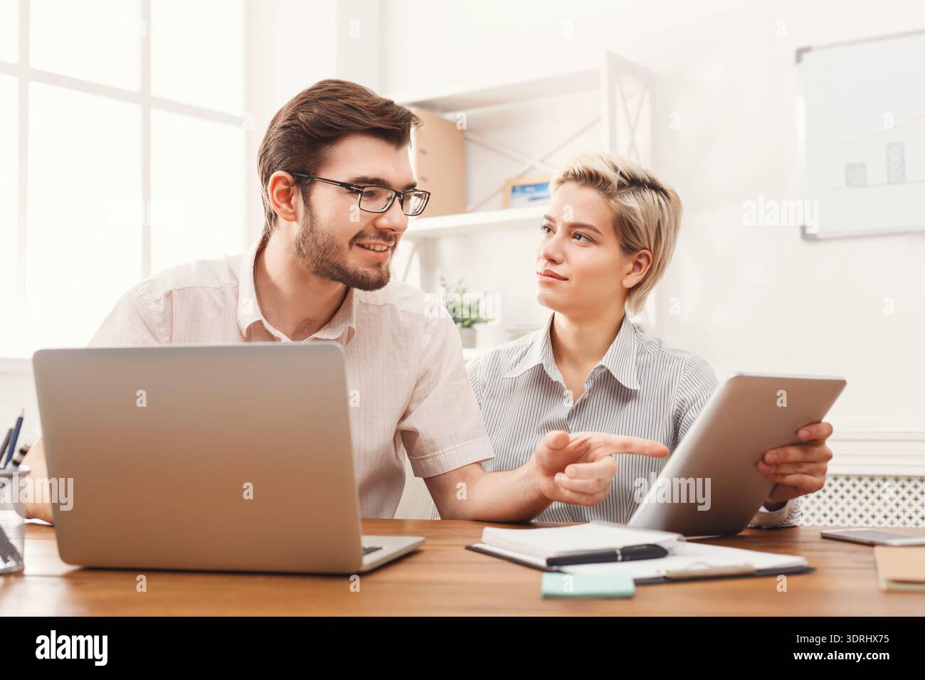People Work Together on a Project Using Laptops and a Tablet in a Bright Office Setting Stock Photo