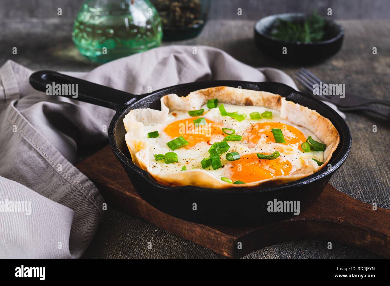 Homemade scrambled eggs in pita bread with herbs in a frying pan on the table Stock Photo