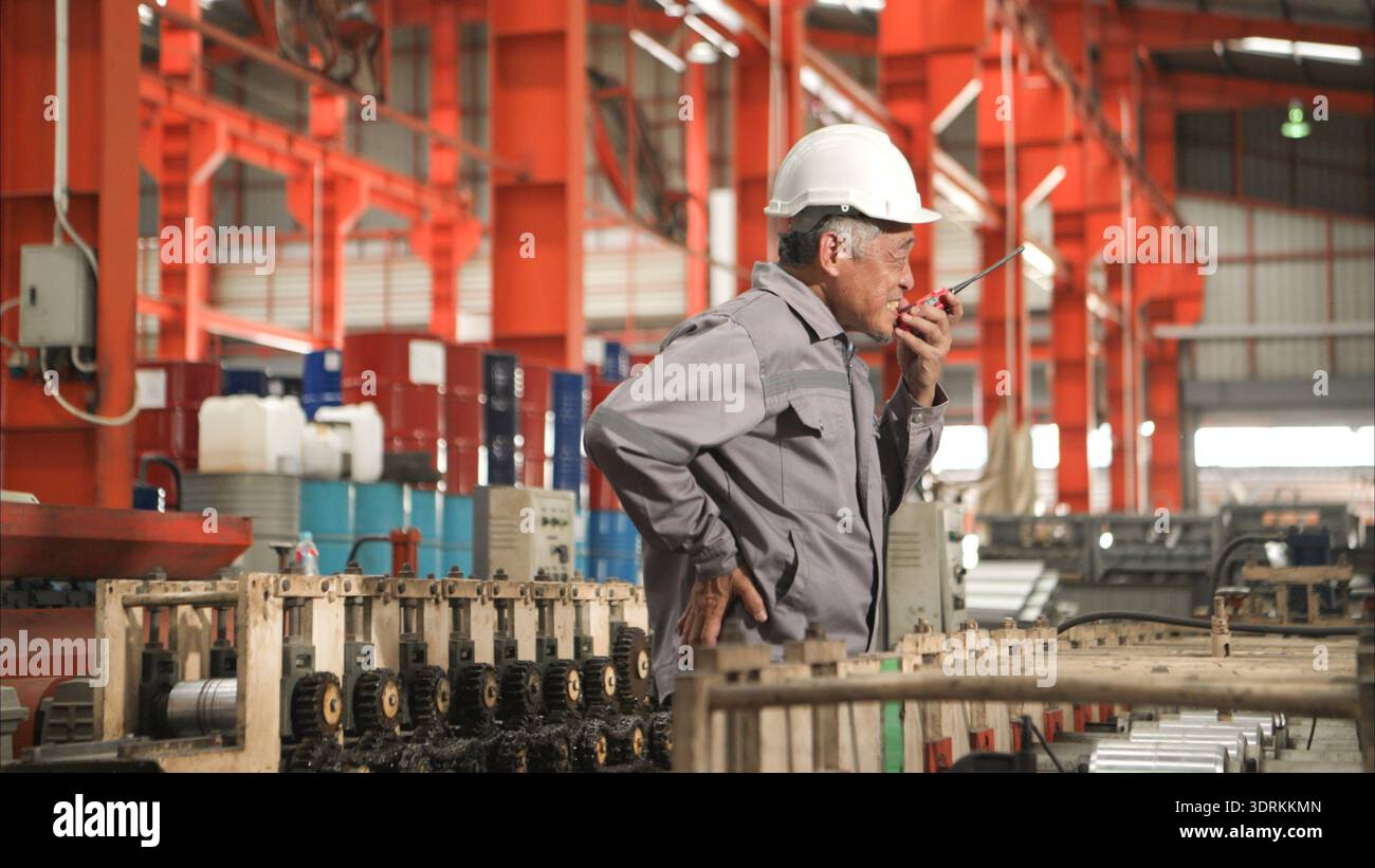 Industrial worker in protective gear experiencing back pain while working on factory machinery Stock Photo