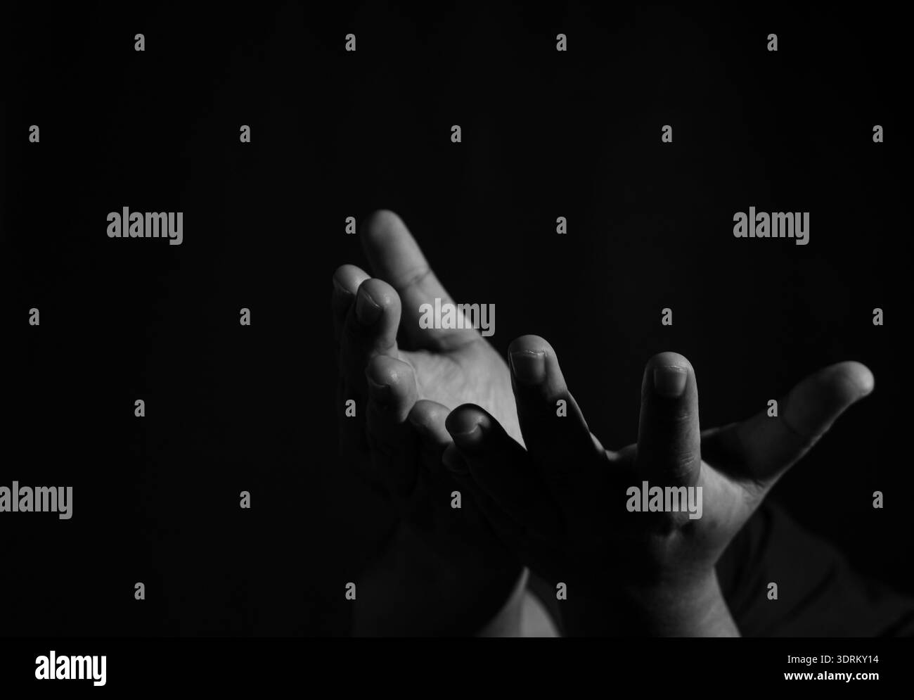 Black and white dramatic shot of open hand reaching upward, expressive gesture symbolizing hope, offering, support and emotional connection. Stock Photo