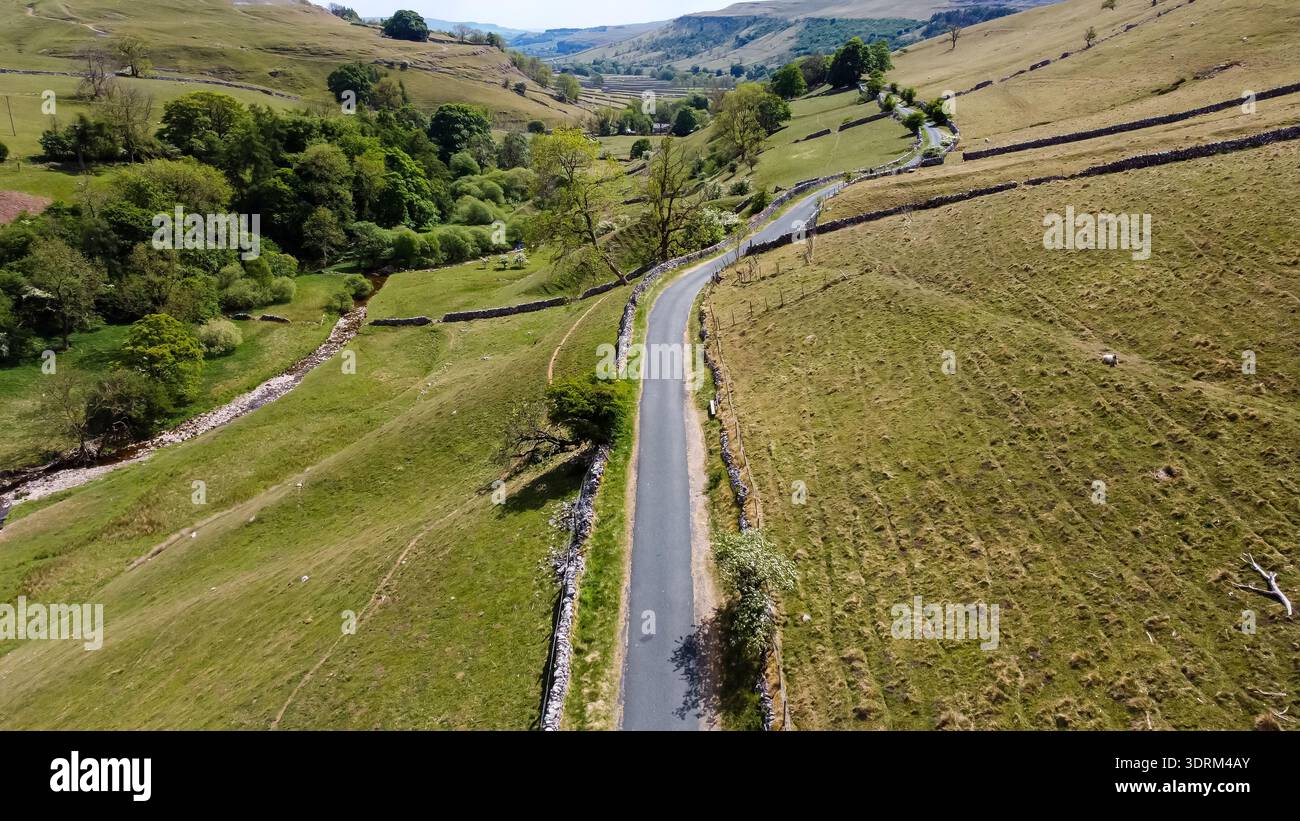 Aerial view of a winding asphalt road cutting through a green rural ...