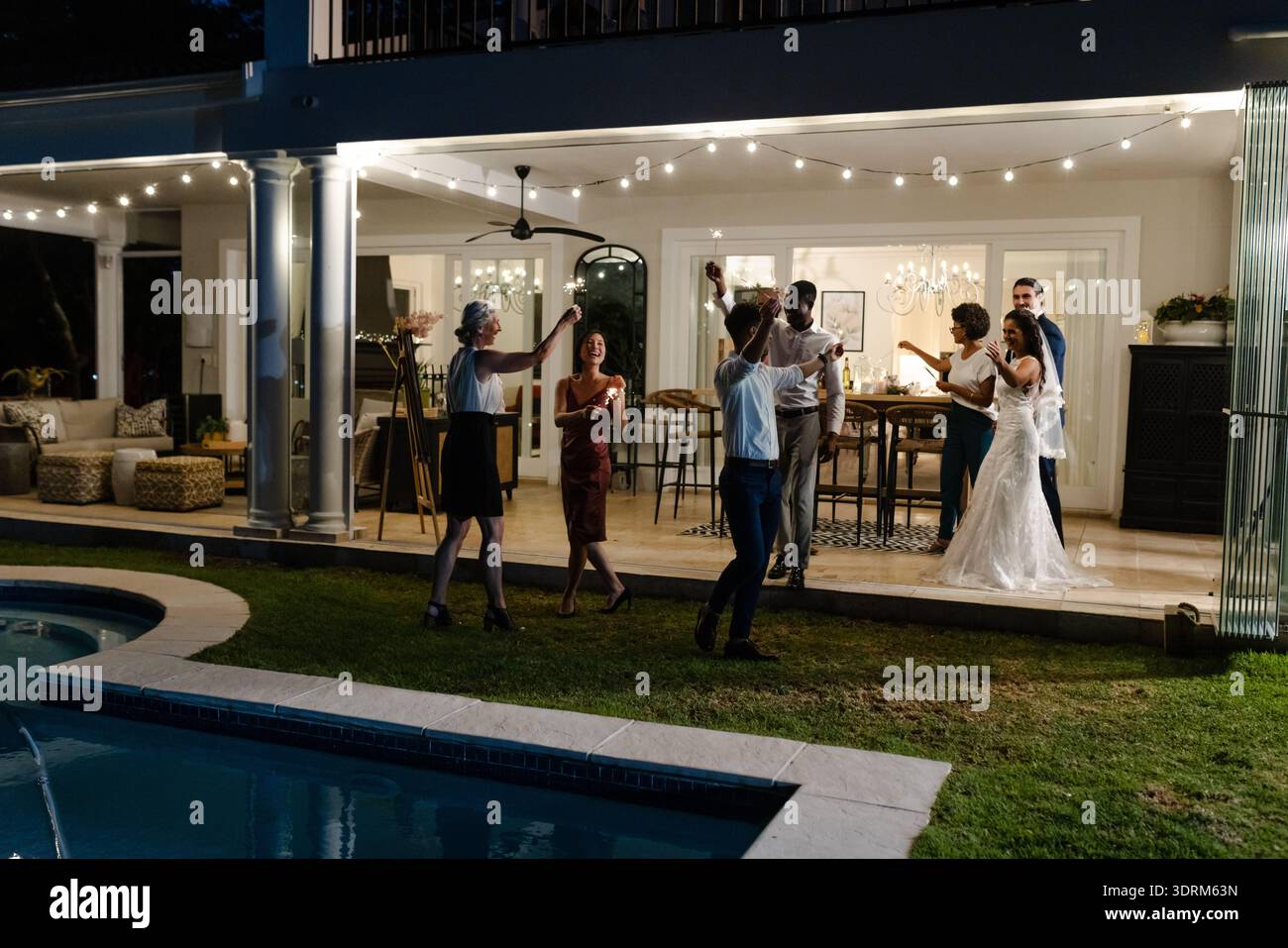 Celebrating joyfully, guests at outdoor wedding reception near pool with string lights. celebration, festive, poolside Stock Photo