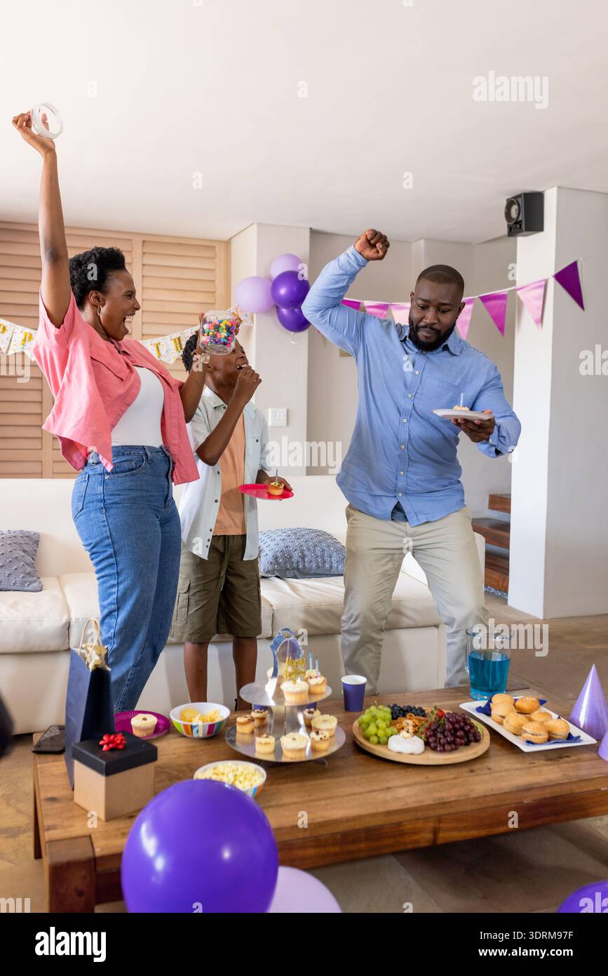 Celebrating at home, family dancing joyfully around table with snacks ...