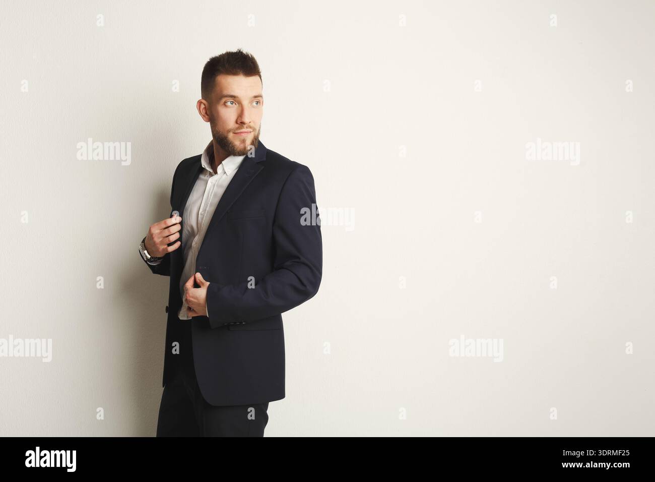 A Man Stands Confidently Against a Light Wall Stock Photo