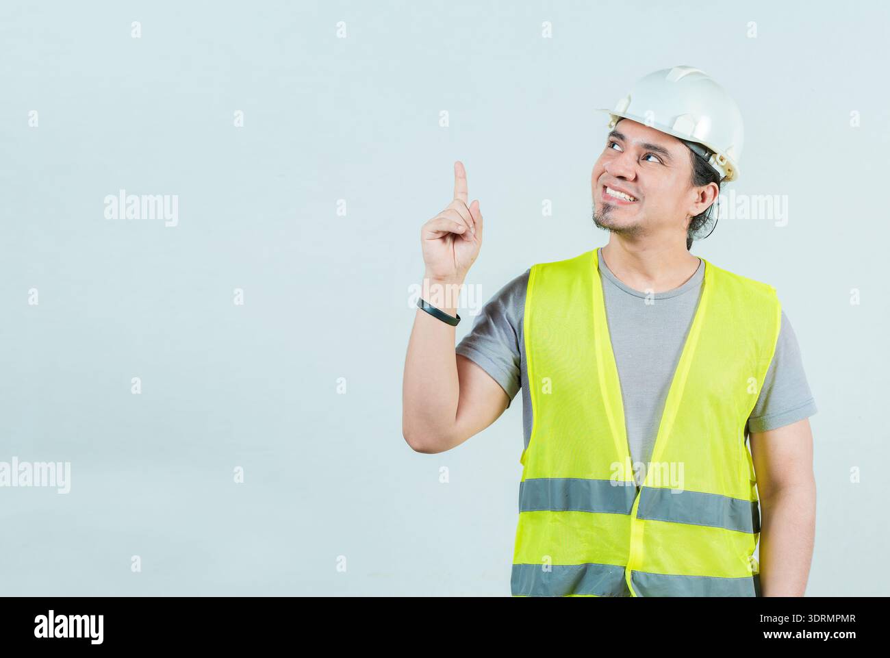 Smiling engineer pointing up isolated. Happy young builder with helmet pointing up Stock Photo