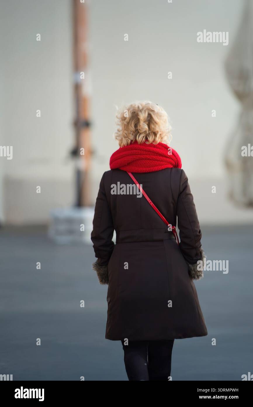 blonde senior woman with red scarf walking on the street in alghero view from behind Stock Photo