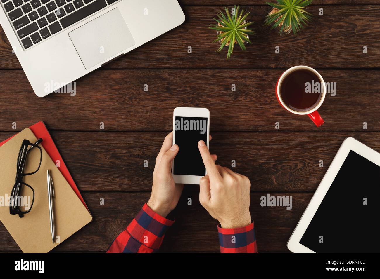 Collection of Devices and Materials on a Wooden Table With an Individual Using a Smartphone Stock Photo