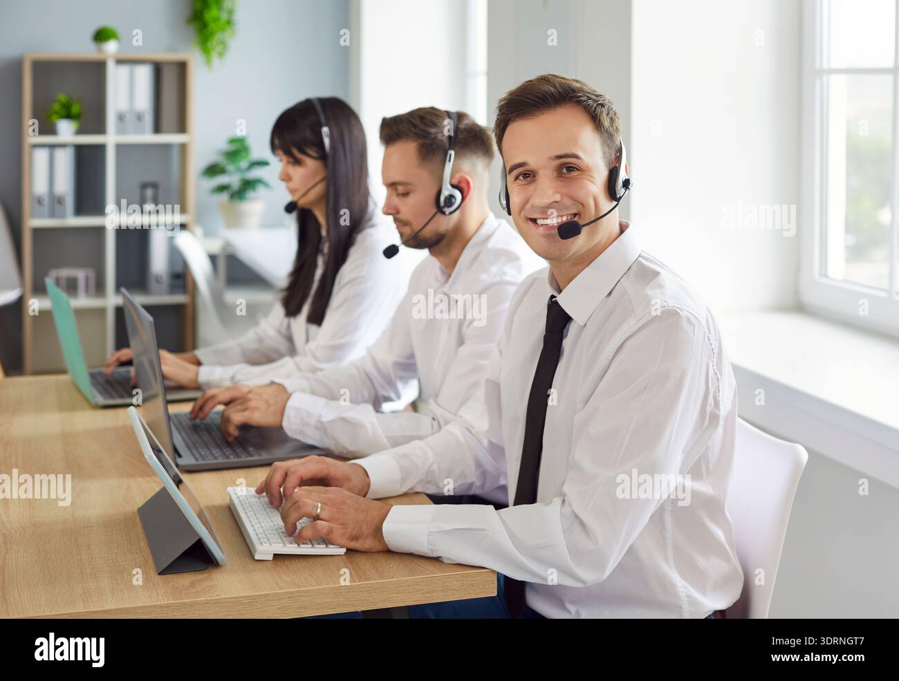 Smiling callcenter team using headsets and laptops while providing customer support Stock Photo