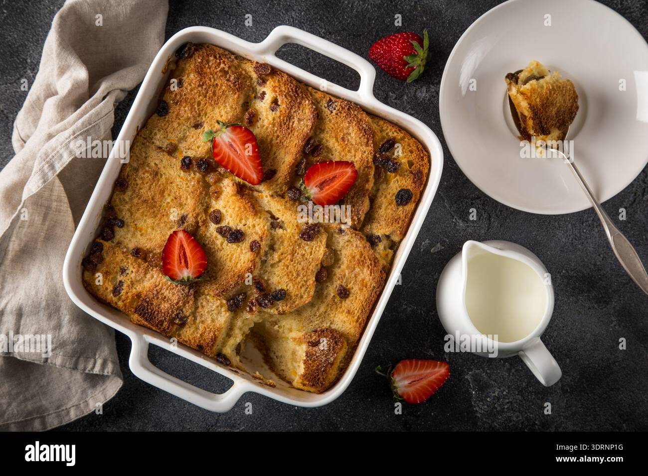 Bread and butter pudding with raisins and fresh strawberry in white baking dish Stock Photo