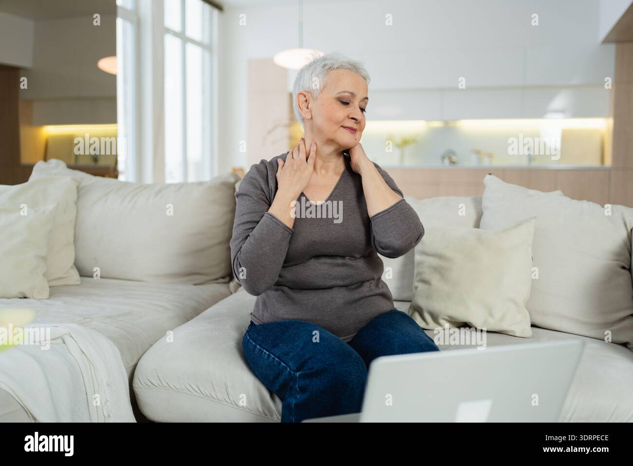 Middle aged senior woman at home relaxing stretching hands and body taking break from work on laptop. Older mature woman happy a Stock Photo