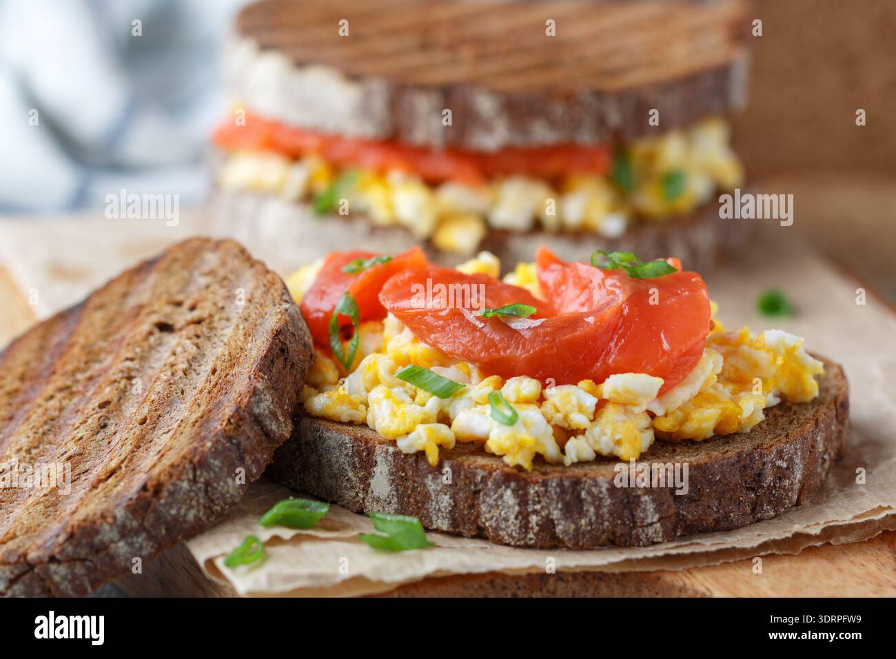 Scrambled eggs and smoked salmon on rye bread with green onions. A sandwich for breakfast. Selective focus Stock Photo