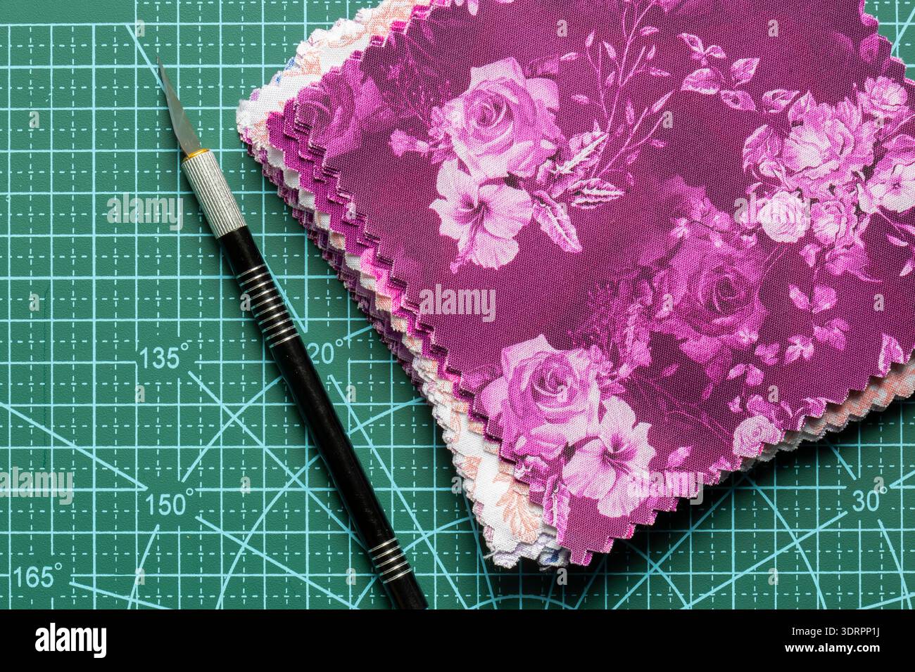 Fabric patchwork quilting patterned quilting squares on a green cutting mat with a craft knife background backdrop. Stock Photo