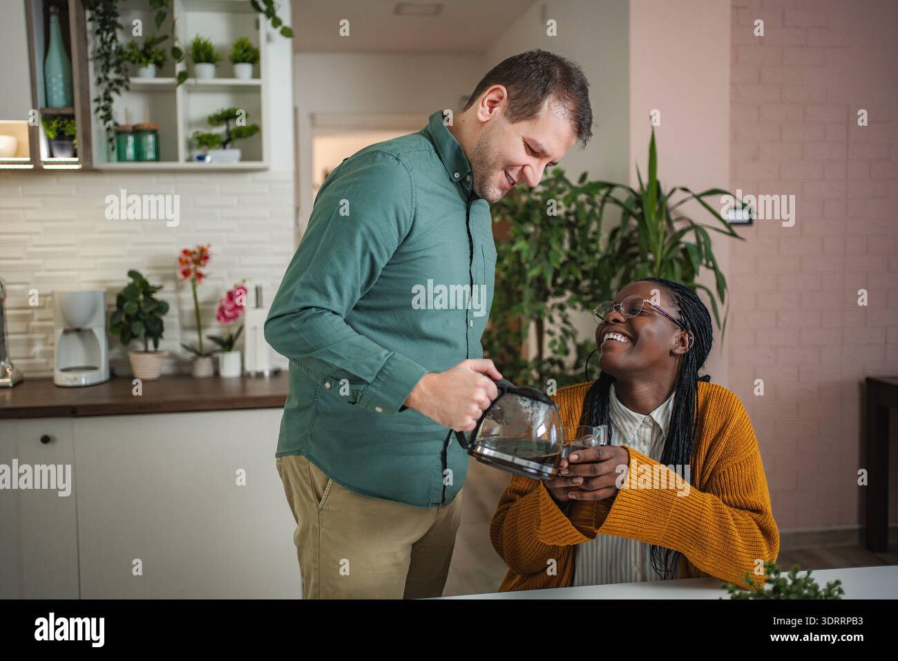 Man pouring coffee for laughing woman in kitchen Stock Photo