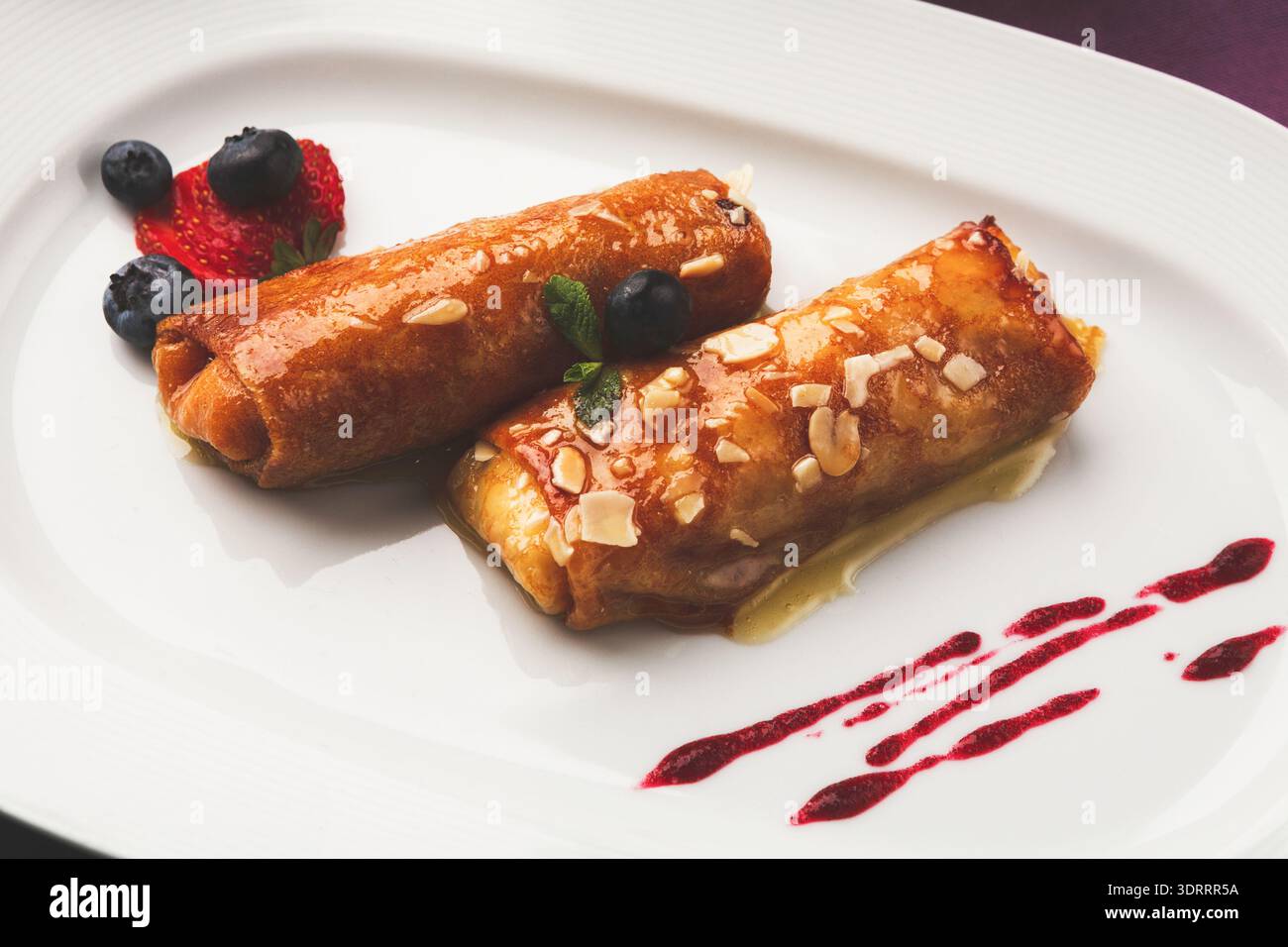 Desserts Arranged on a White Plate With Fruits and Sauce on a Simple Background Stock Photo