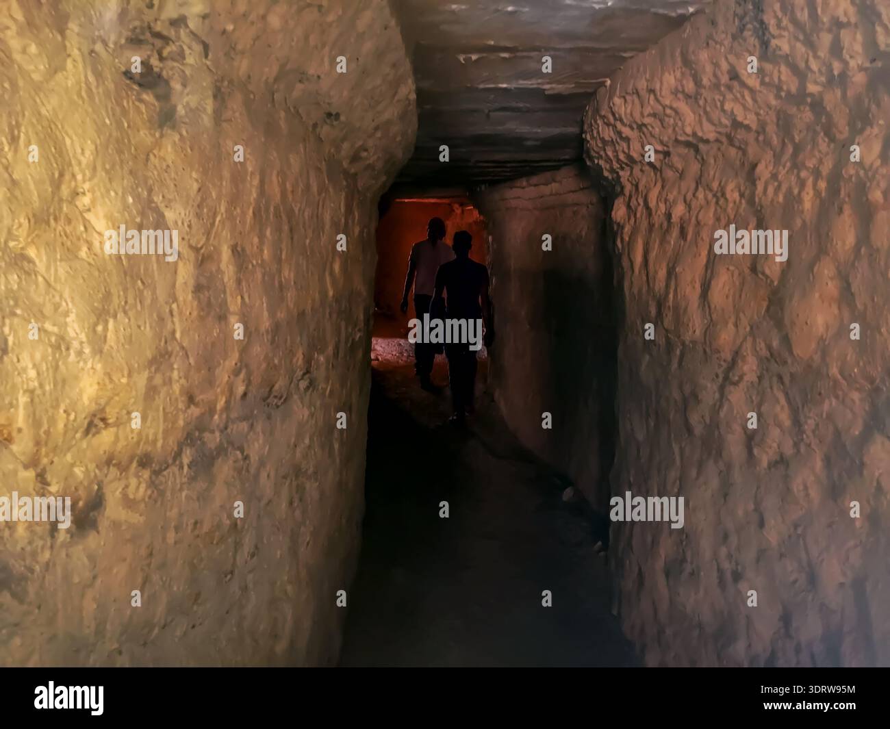 Two male silhouettes go into a dark cave, view from the back. Dark stone narrow corridor, background with copy space - Smartphone Captured Stock Image