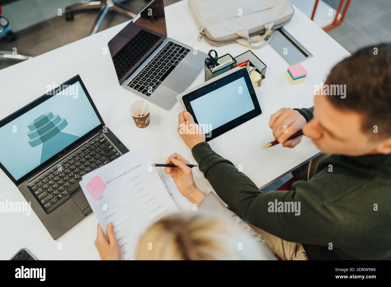 Teamwork in a modern office: two people collaborate using laptops, tablet, and documents at desk Stock Photo