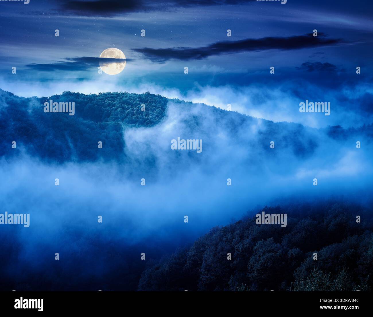 mountain landscape with cold fog at night. low clouds evaporating over the forested hill in full moon light. outdoor scenery in spring for remote high Stock Photo