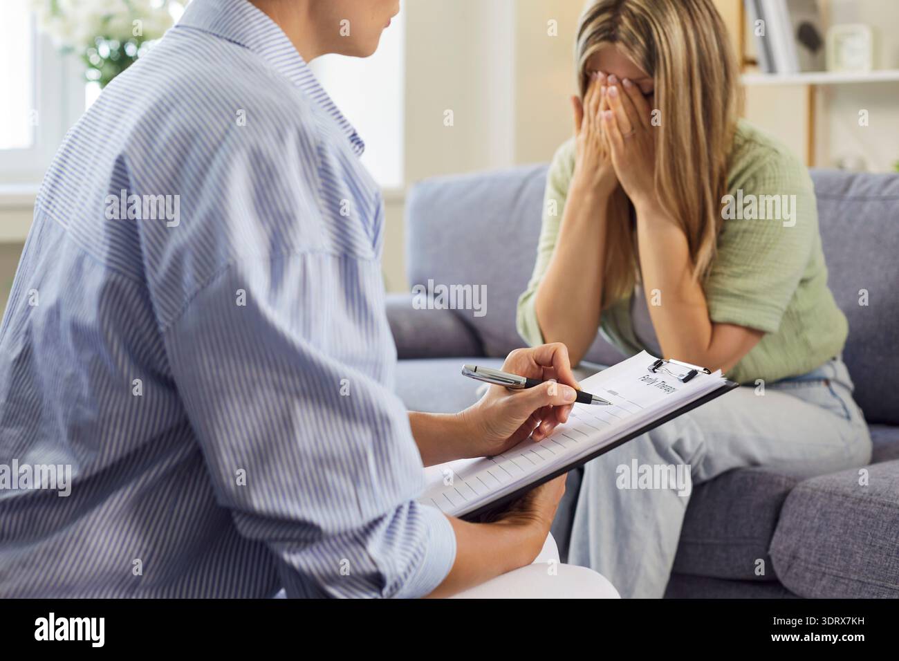 Psychologist writing notes as upset patient covers face during counseling session Stock Photo
