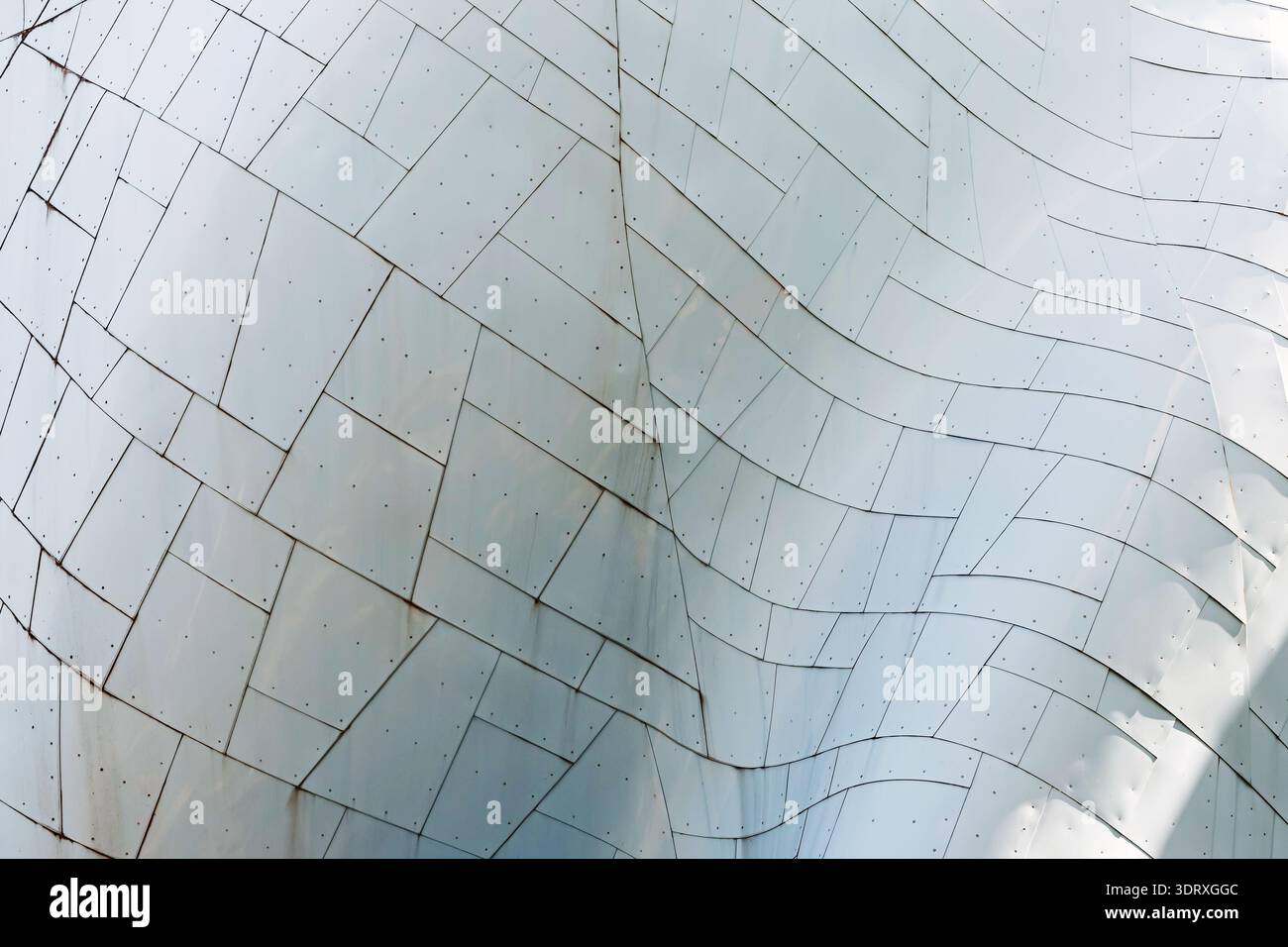 Abstract close-up of curved metal facade with tiled panels, seams, and rivets; modern architecture texture in cool tones, minimal background for desig Stock Photo