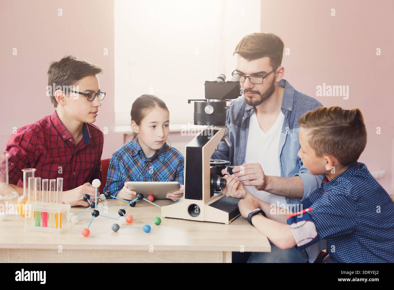 Students Learn About Science With a Teacher Using a Microscope During a Class Activity Stock Photo