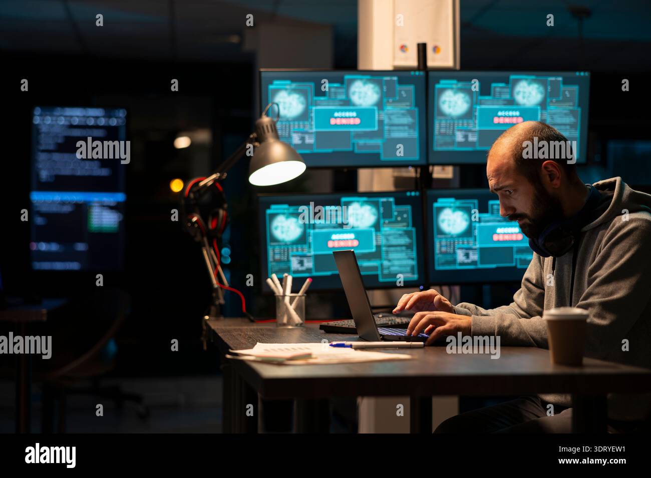 Dedicated male programmer analyzing system data and writing secure code on laptop. Concentrated developer enhancing cloud computing protection and addressing cybercrime risks during night shift. Stock Photo