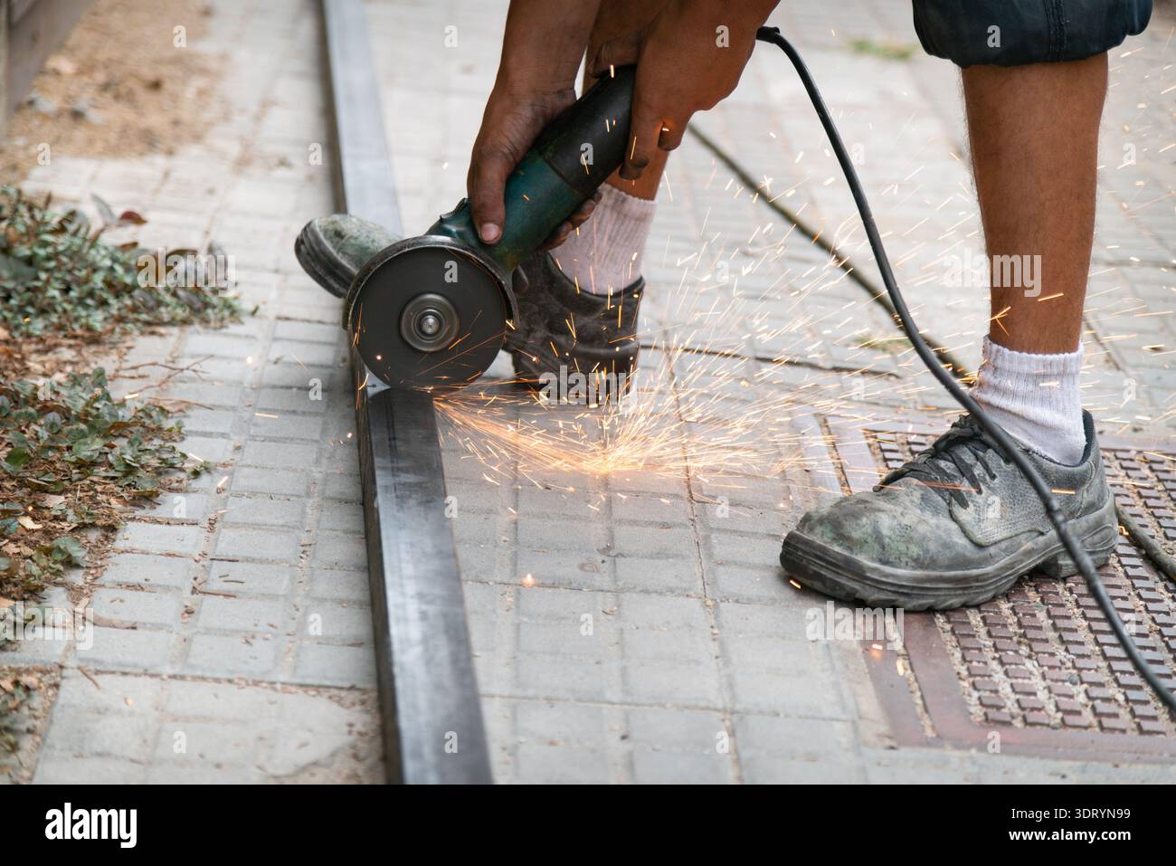 Worker using an angle grinder to cut a metal profile, creating sparks Stock Photo