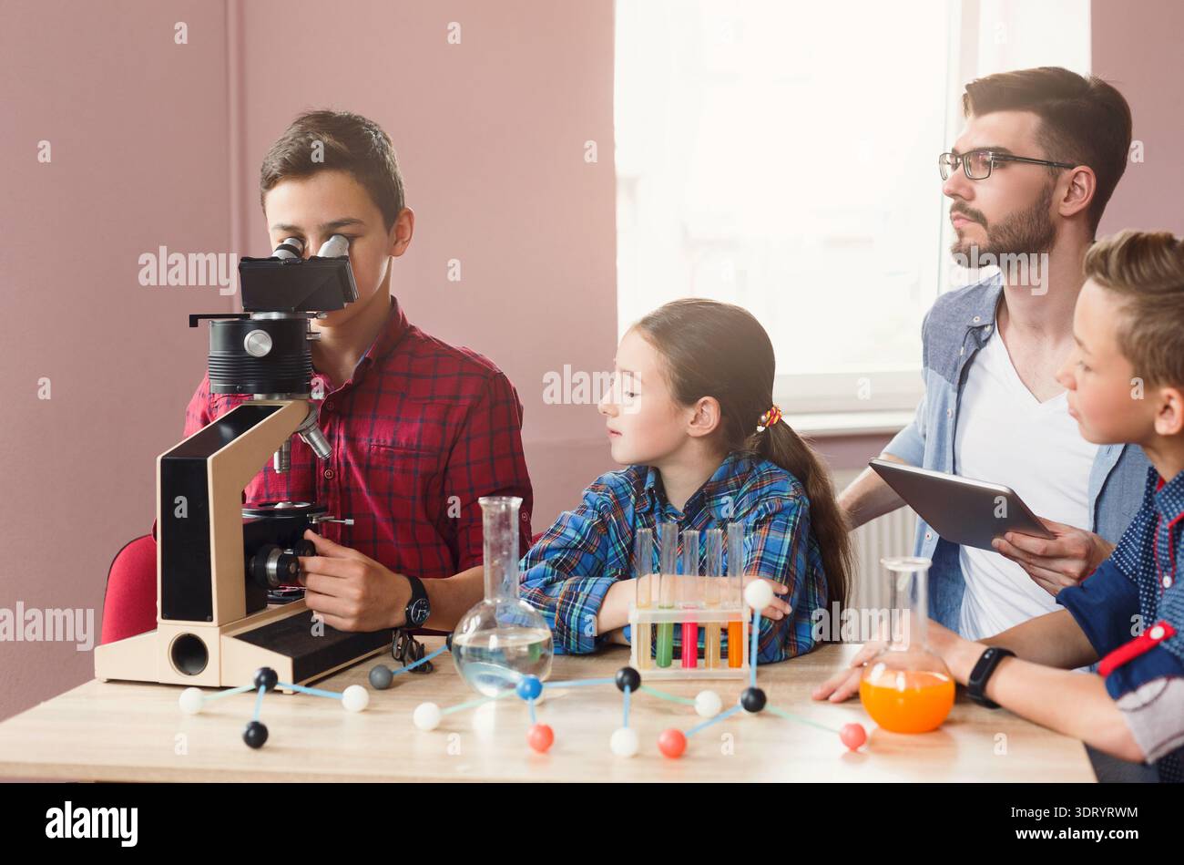Students Learn About Science and Have Fun Using a Microscope in a Classroom During the Afternoon Stock Photo