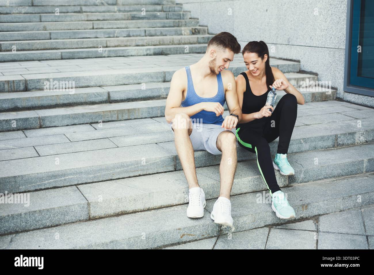Couple Sits on Steps After Workout Sharing Snacks and Drinks While Relaxing Outside Stock Photo