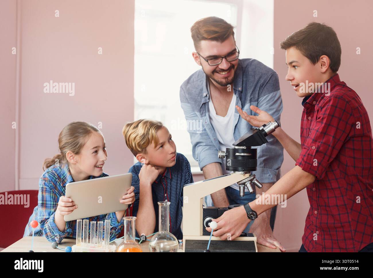 Students Learn About Science With Teacher Using Microscope and Equipment in Classroom Setting Stock Photo
