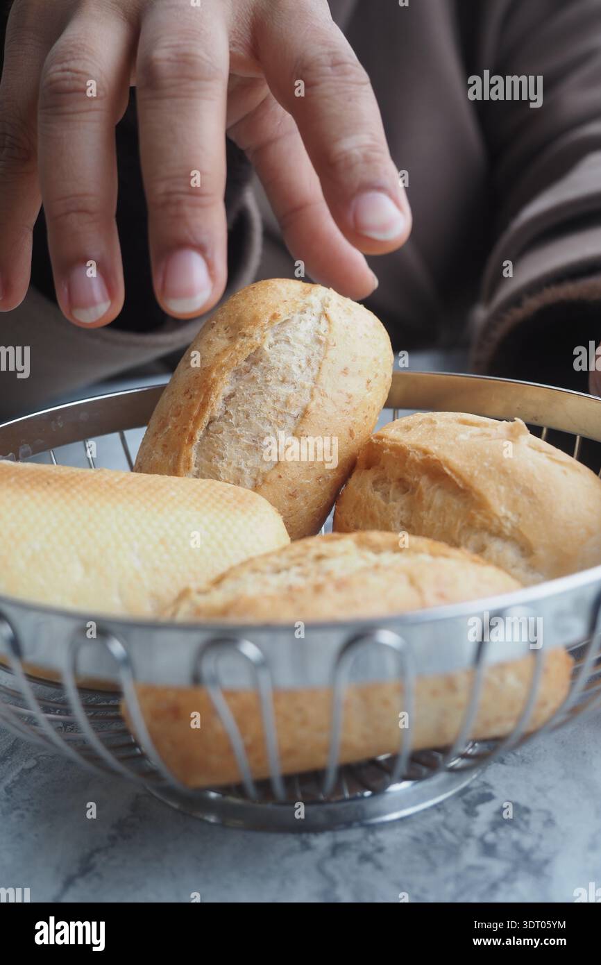 Hand reaching for bread rolls in a bowl on a table Stock Photo