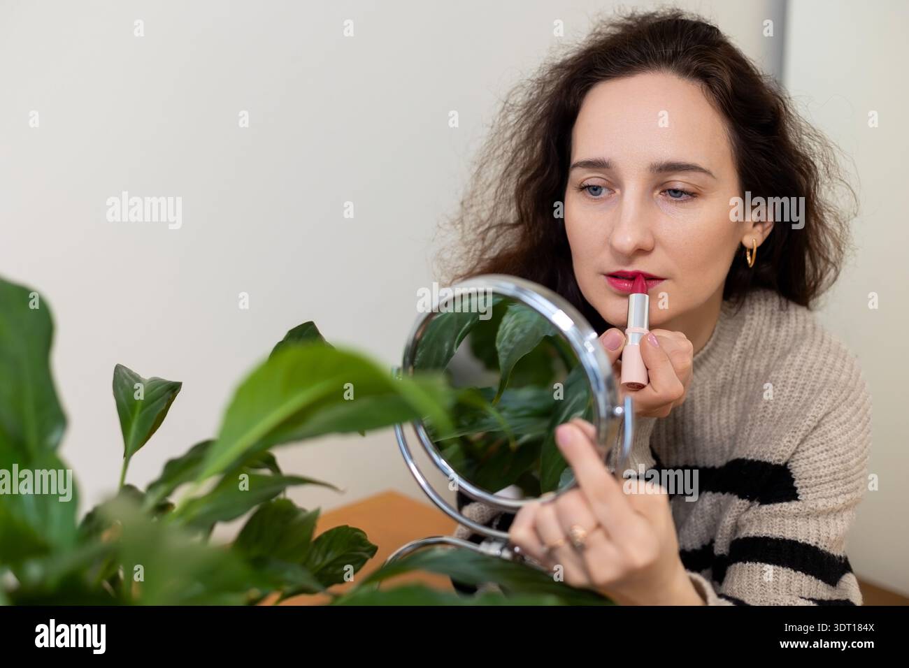 Woman applying lipstick using handheld mirror. Space for text. Stock Photo