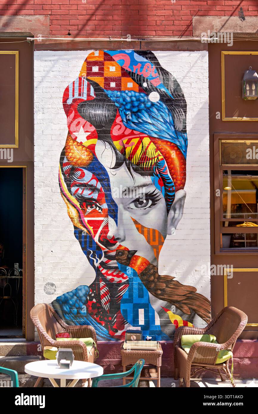 Visitors enjoy the sunny day at a cafe in Little Italy, while admiring the Audrey Hepburn mural on the wall next door. Stock Photo