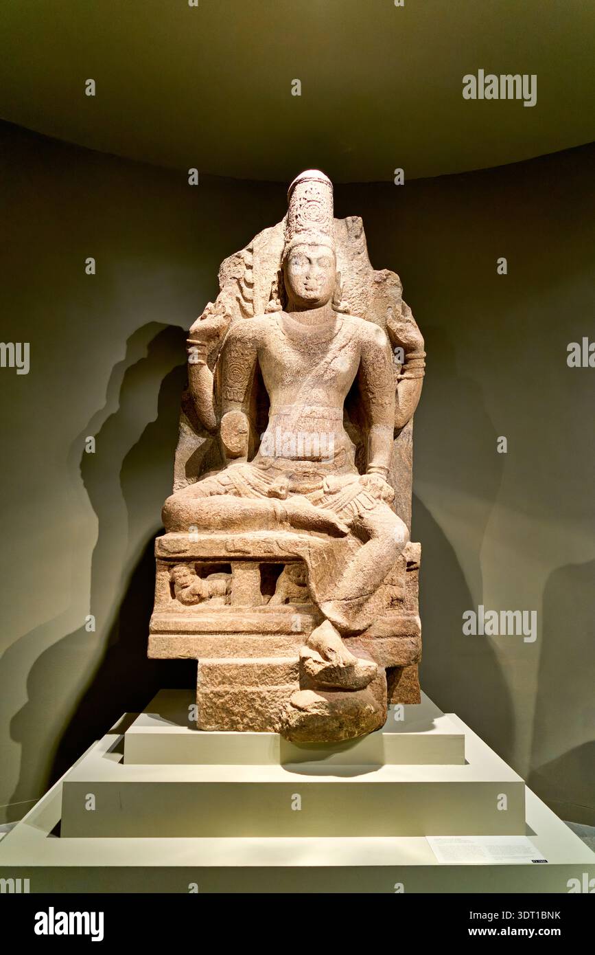 A statue of a seated figure is displayed in the Asian Art Gallery in Manhattan. Visitors view the artwork in a well-lit setting. Stock Photo